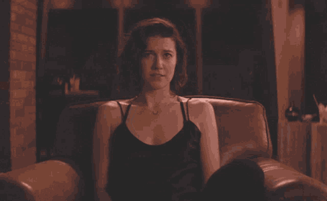 a woman in a black tank top is sitting in a leather chair