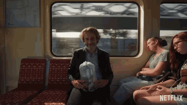 a man sitting on a train with a bag in his hand and a netflix logo on the bottom right