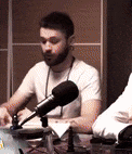 a man with a beard is sitting in front of a microphone .