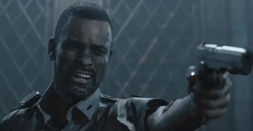 a man in a uniform is pointing a gun at the camera in a dark room .