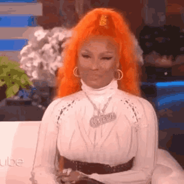 a woman with orange hair is sitting on a couch wearing a white shirt and earrings .