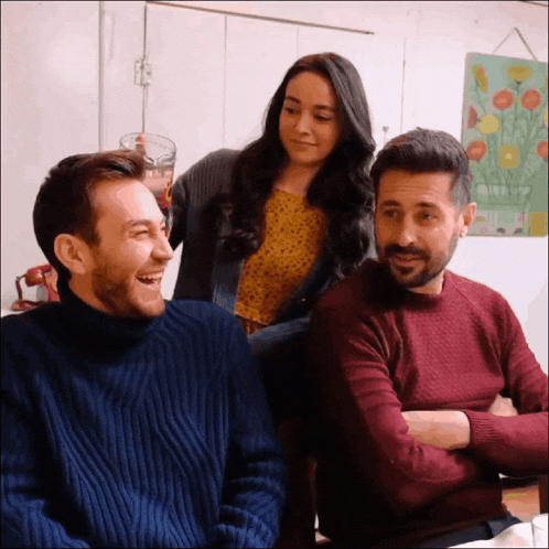 a man in a blue sweater is laughing with a woman and a man in a red sweater