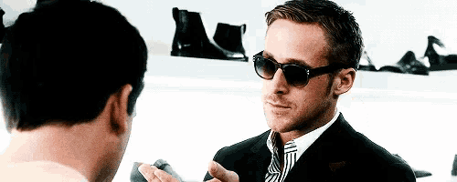 a man wearing sunglasses and a suit is talking to another man .