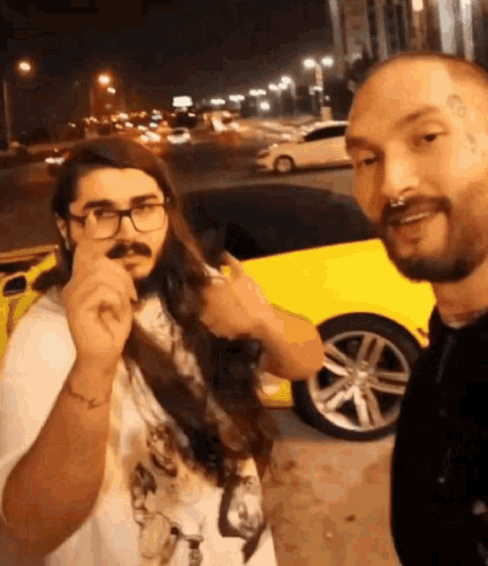 a man with glasses and a beard is standing next to another man with long hair