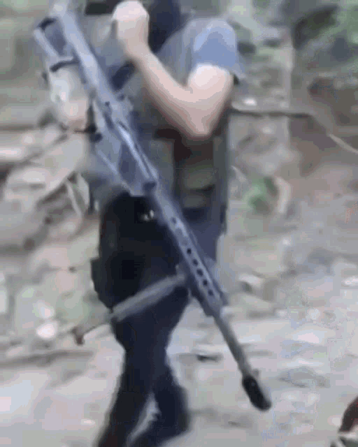 a man is holding a large rifle in his hand while walking down a dirt road .