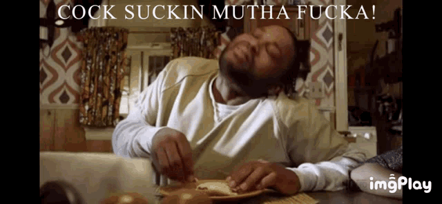 a man sitting at a table with the words cock suckin mutha fucka on the bottom