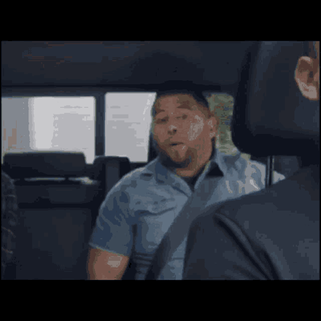a man in a blue shirt with the letter u on it is sitting in the back of a car