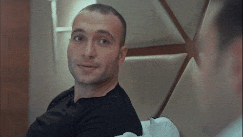 a man in a black shirt sits on a bed