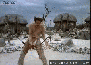 a man without a shirt is holding a spear in front of a village .