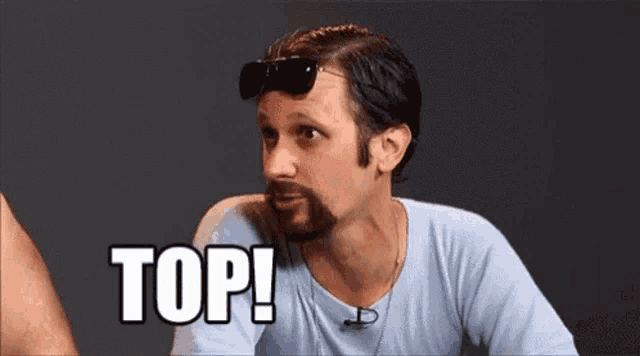 a man with a beard wearing sunglasses and a light blue shirt is saying top .
