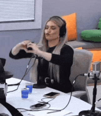 a woman wearing headphones is sitting at a table with a microphone and a cell phone .