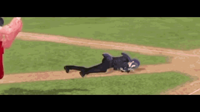 a man is laying on the ground on a baseball field while a woman throws a ball .