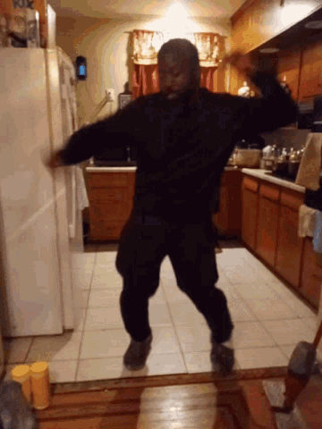 a man is dancing in a kitchen with a white refrigerator in the background