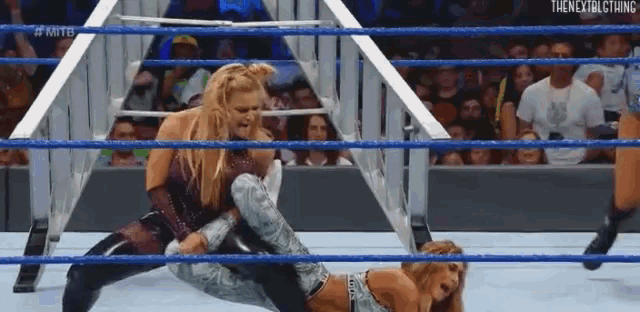 two women are wrestling in a wrestling ring while a crowd watches .