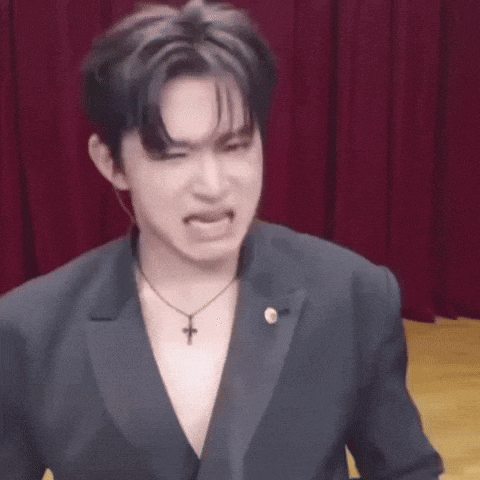 a man wearing a suit and a cross necklace is making a face .