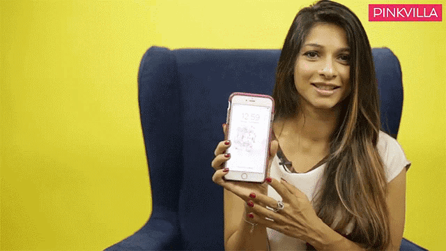 a woman sitting in a chair holding a cell phone with the time 12:59 on it