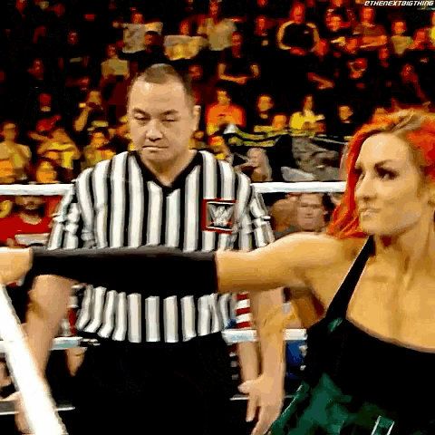 a woman in a green dress is standing next to a referee in a wrestling ring