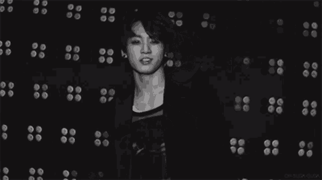 a black and white photo of a man dancing in front of a wall of flowers .