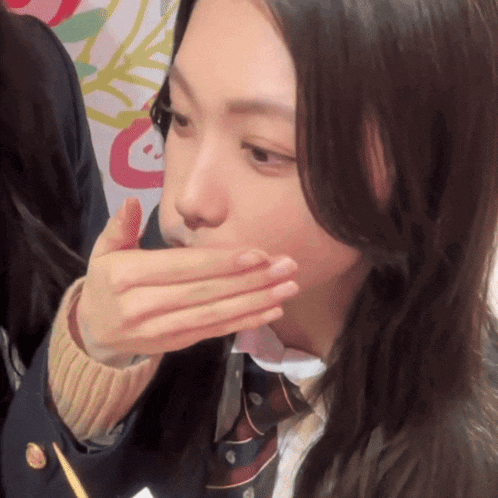 a woman covering her mouth with her hand while wearing a school uniform