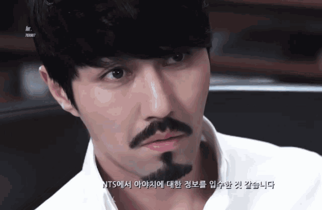 a man with a mustache and a white shirt is looking at the camera