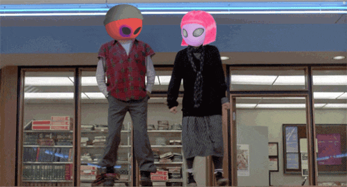 a man and a woman wearing alien masks stand in front of a book store