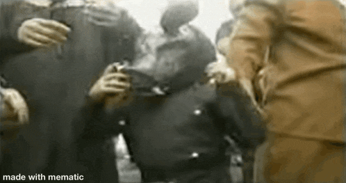 a black and white photo of a group of people standing around a man holding a gun .