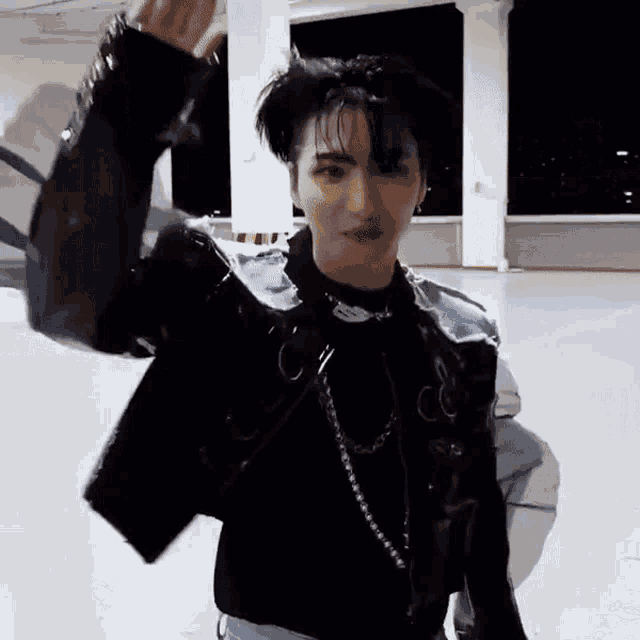 a young man wearing a black jacket and a black sweater is waving his hand .