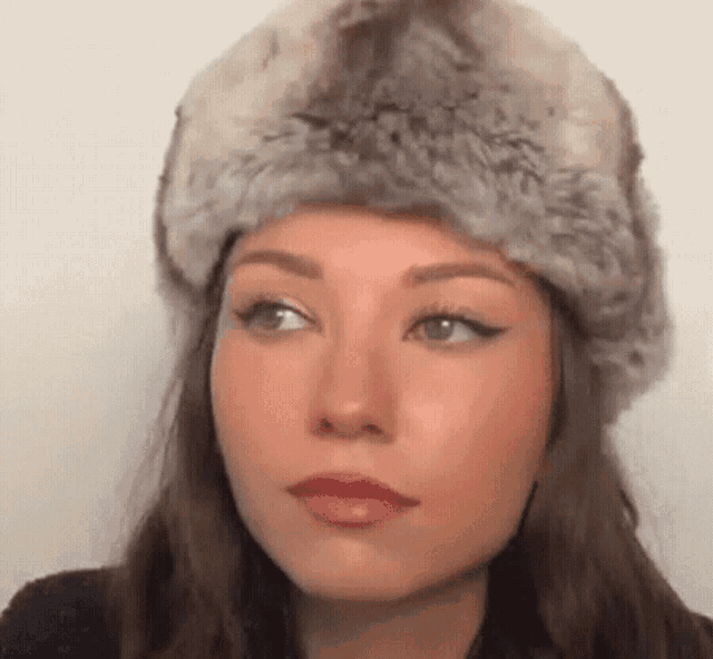 a woman is wearing a fur hat and looking at the camera