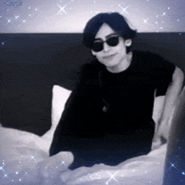 a man wearing sunglasses and a black shirt is laying on a bed