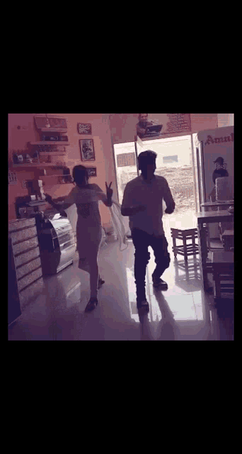 two men are dancing in a room with a refrigerator that says amul