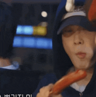 a man is eating a sausage on a stick while another man looks on .