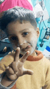 a young boy with white paint on his face giving the peace sign