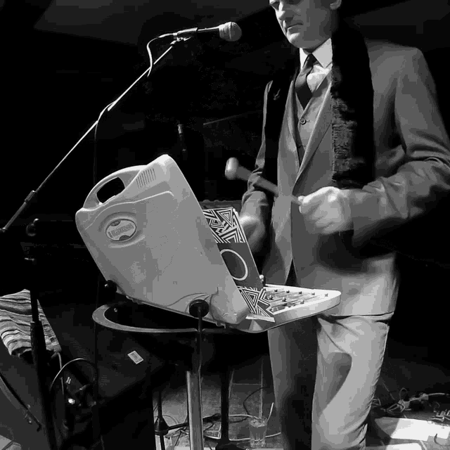 a man in a suit is playing a keyboard and a microphone while holding a box that says " alex "