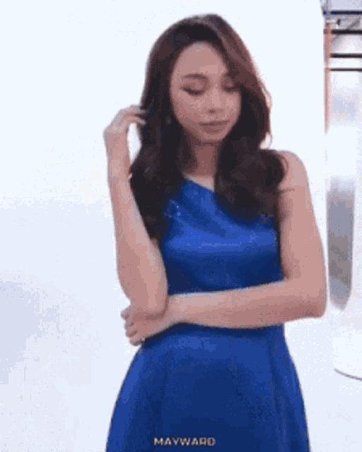 a woman in a blue dress is standing with her hands folded .