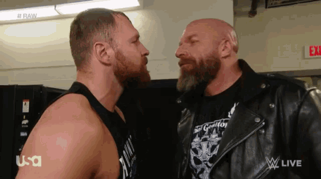 two men are facing each other in a room with a red exit sign in the background
