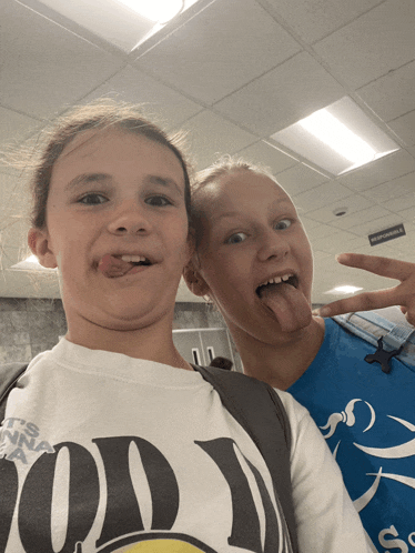 two girls sticking their tongues out and one is wearing a shirt that says ' good ' on it