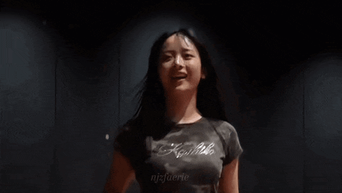 a young woman is standing in a dark room with her arms in the air and laughing .