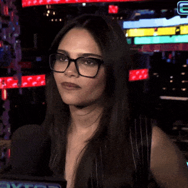 a woman wearing glasses stands in front of a microphone with the letter e in the corner
