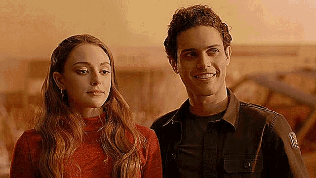 a man and a woman are standing next to each other and smiling . the woman is wearing a red sweater .