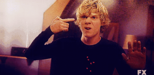 a young man with blonde hair is pointing at his head .