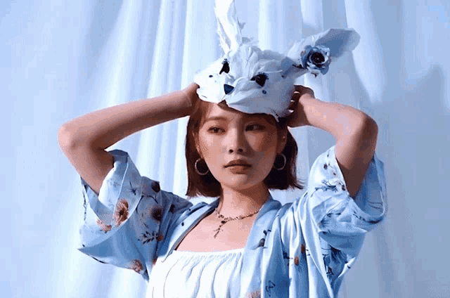 a woman wearing a blue floral shirt has a paper rabbit headpiece on her head