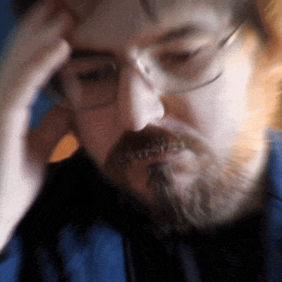 a man with glasses and a beard holds his hand to his head