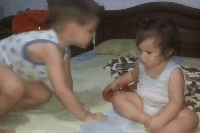 two little girls are playing on a bed and one is wearing a diaper