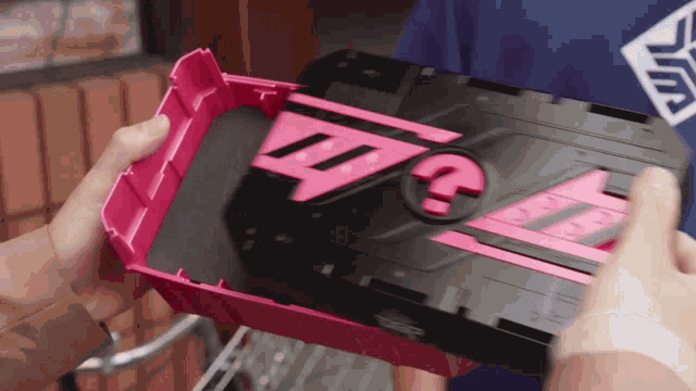 a person is holding a pink and black object with the letter g on it