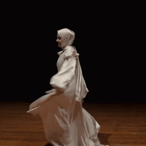 a woman in a white dress and hijab is dancing on a stage