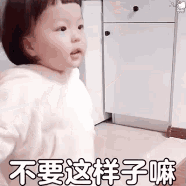 a baby is standing in front of a white cabinet and making a face .