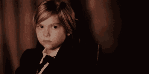 a young boy in a suit and tie is sitting in a chair and looking at the camera .