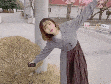 a woman leaning against a pole with her arms outstretched while holding a cell phone