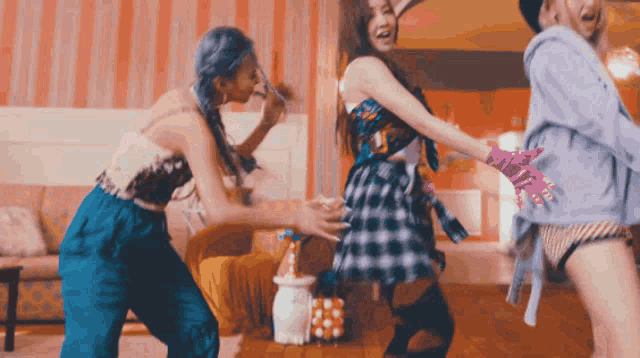 three women are dancing in a living room and one of them is wearing a plaid dress