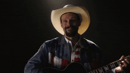a man in a cowboy hat is playing a guitar in front of a large american flag